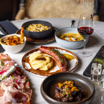Assiette gourmande avec saucisse, purée, spécialités savoyardes et verre de vin rouge