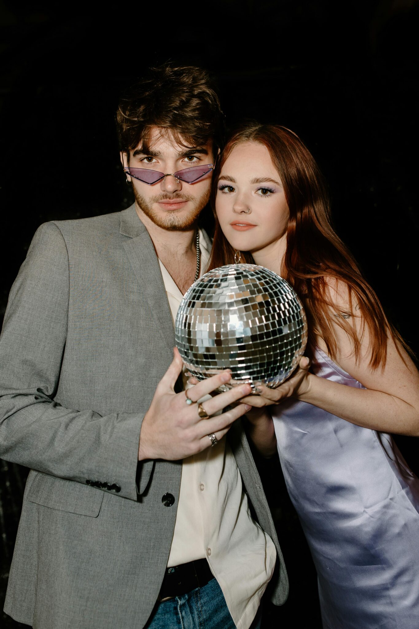 Un homme et une femme en tenue de soirée posant sous une boule disco aux Chalets des Praz à La Clusaz